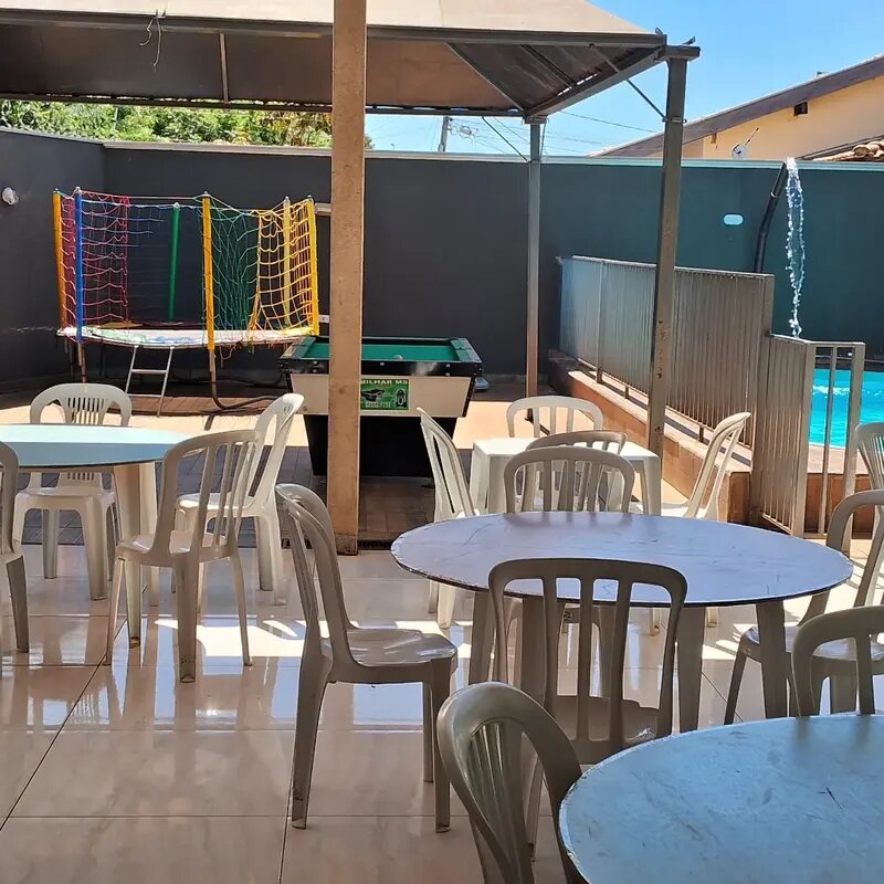 Espaço externo da Mimo Casa de Festa com mesas, cama elástica, mesa de sinuca e piscina visíveis ao fundo